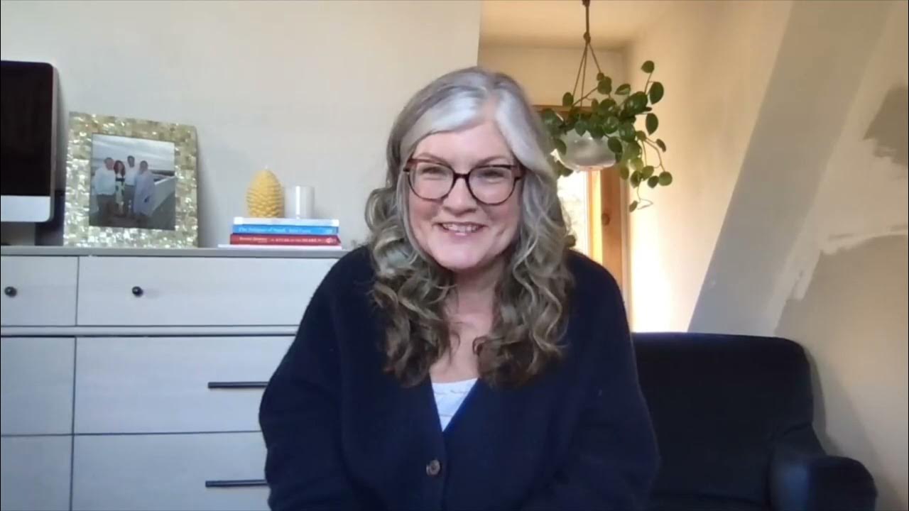 Janet smiling while sitting in her office chair wearing big glasses