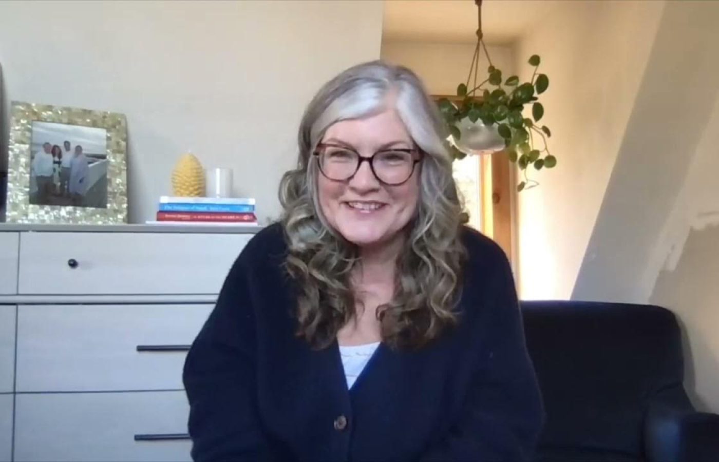 Janet smiling while sitting in her office chair wearing big glasses